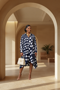 Model wearing navy polka dot long sleeve shirt dress with asymmetric hem and gold accessories